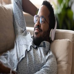 Serene satisfied young adult african american man lying on comfortable sofa wear wireless headphones enjoy listen modern music audio book with eyes closed meditate relax feel no stress chill at home